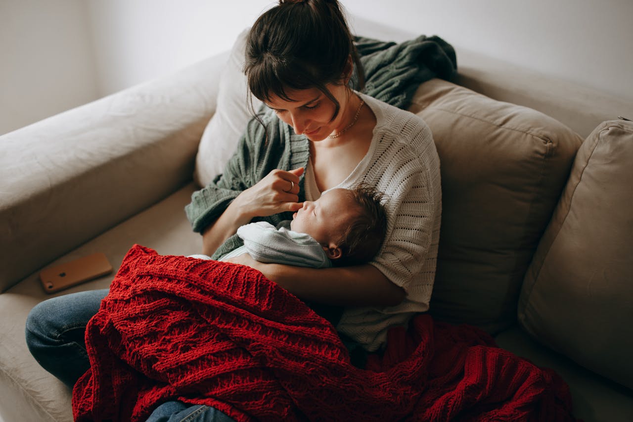 Tender moment between a mother and her baby wrapped in a blanket on a cozy sofa indoors.